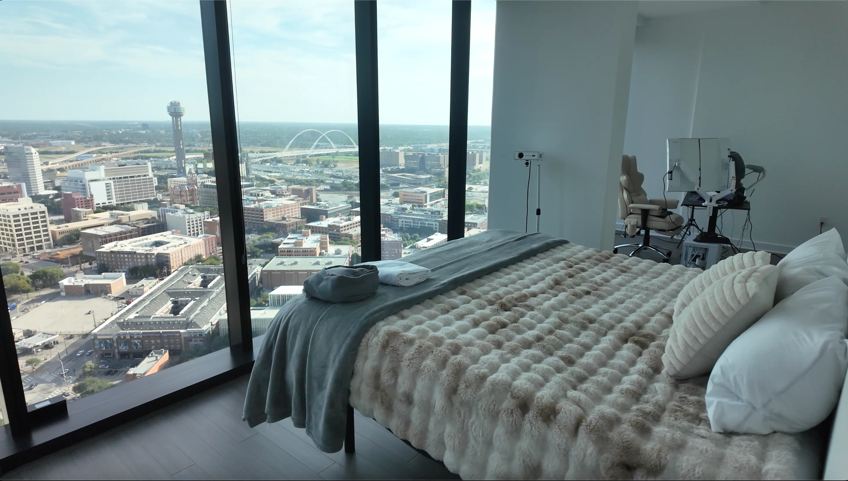 A tidy bedroom with a made bed and a floor-to-ceiling view of the Dallas skyline.