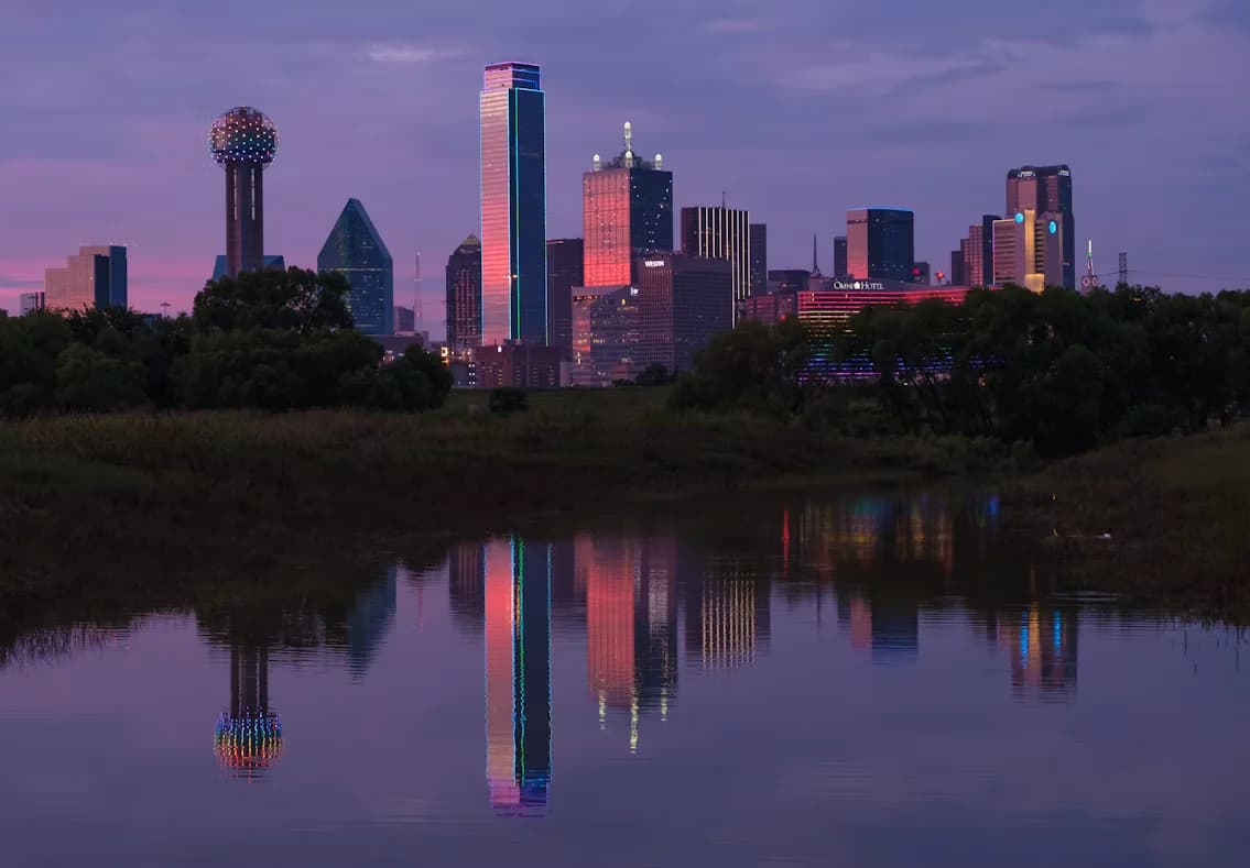 The downtown Dallas skyline at dusk, reflected in the water of the Trinity River.